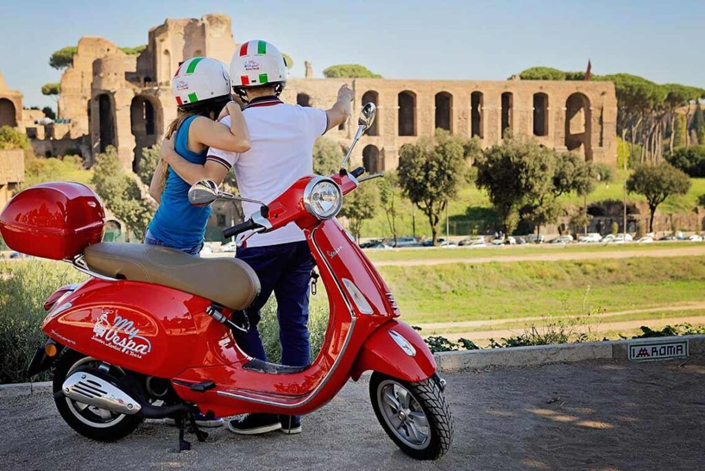 Pareja recorriendo Roma en Vespa frente a ruinas históricas