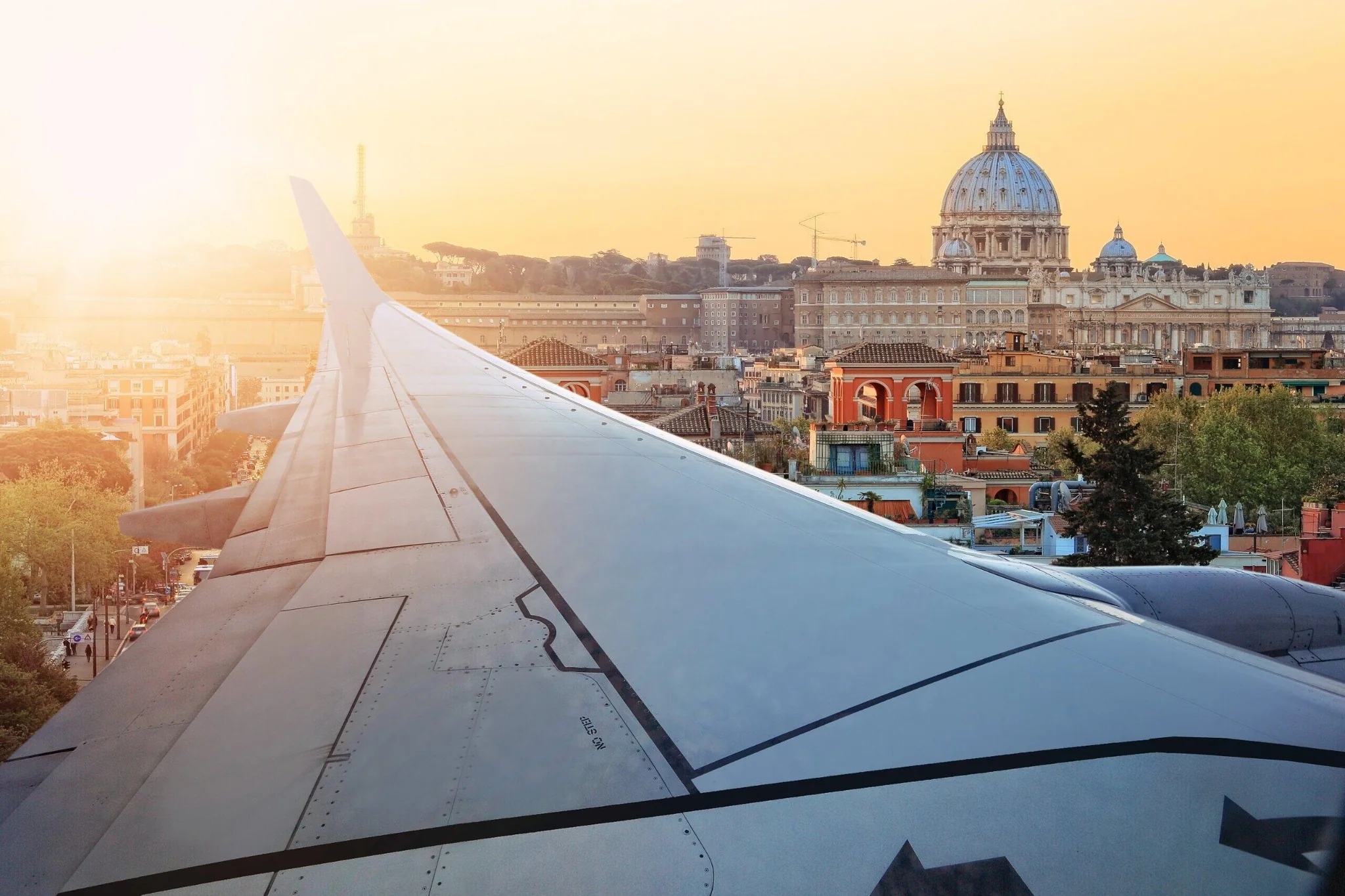 Ala de avión sobre una vista ilustrativa de Roma y la basílica de San Pedro al atardecer
